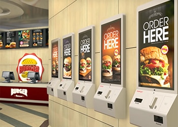 Self Service Kiosks That Say Order Here Lined Up in Burger-Themed Fast Food Restaurant